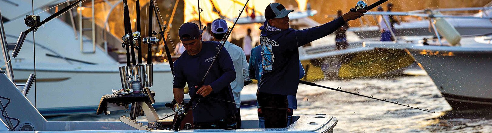 Men fishing from a boat at sunset, casting lines among docked yachts. Background shows splashing water and golden reflections on nearby boats.