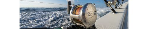 Close-up of a Shimano Talica 40II fishing reel mounted on a boat rod holder. Background shows ocean waves and multiple fishing rods along the boat's rail.