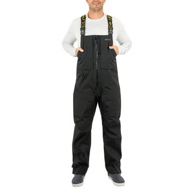 AFTCO Fortress Bib, front view, black bib overalls worn by model with center zipper, chest hand pockets, left hip D-ring, reinforced knee panels, ankle straps, suspenders with strap text "AFTCO" and chest logo "AFTCO"