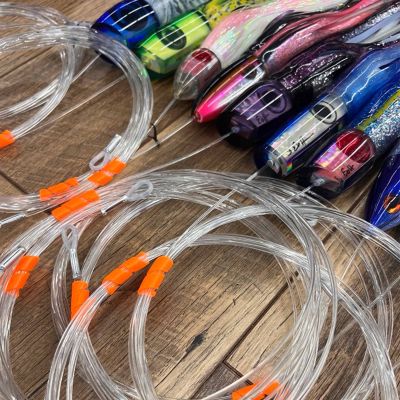 Melton Tackle Leader Keepers in bright orange securing clear coiled leader lines with looped ends. Shown alongside trolling lures for scale; leader and lures NOT included&mdash;demonstration only.