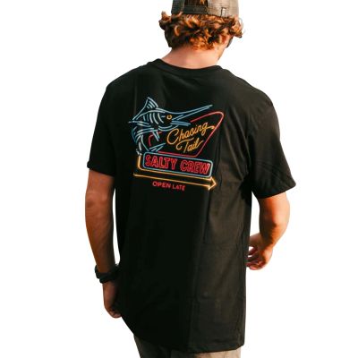 Man wearing Salty Crew Neon Sign T-Shirt in black featuring a neon-style graphic of a marlin fish and text reading “Chasing Tail,” “SALTY CREW,” and “OPEN LATE” in blue, yellow,