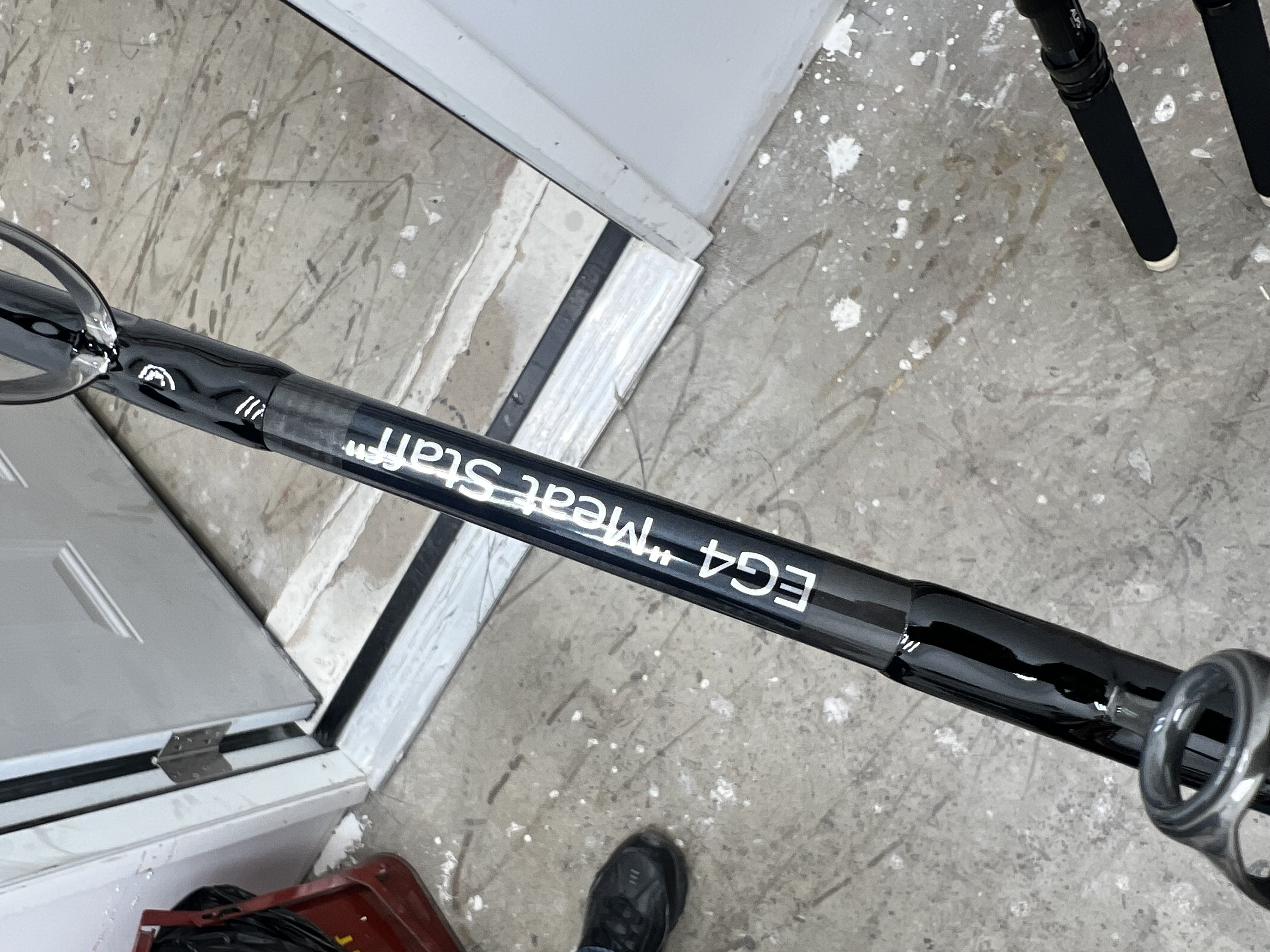 This image shows a custom Melton Tackle Kuro Monster Rail Rod - KR MRR 70XXH rod. The rod is black. It has custom white text EG4"Meat Staff" on the blank.