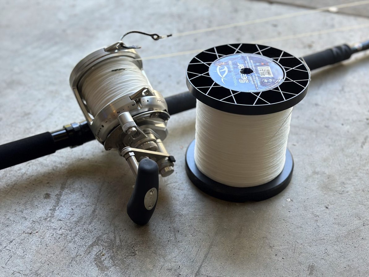 Penn International 50VISXS silver reel mounted on a rod, spooled with white line, sits next to a large spool of Seaguar Threadlock hollow core braid on a concrete surface.