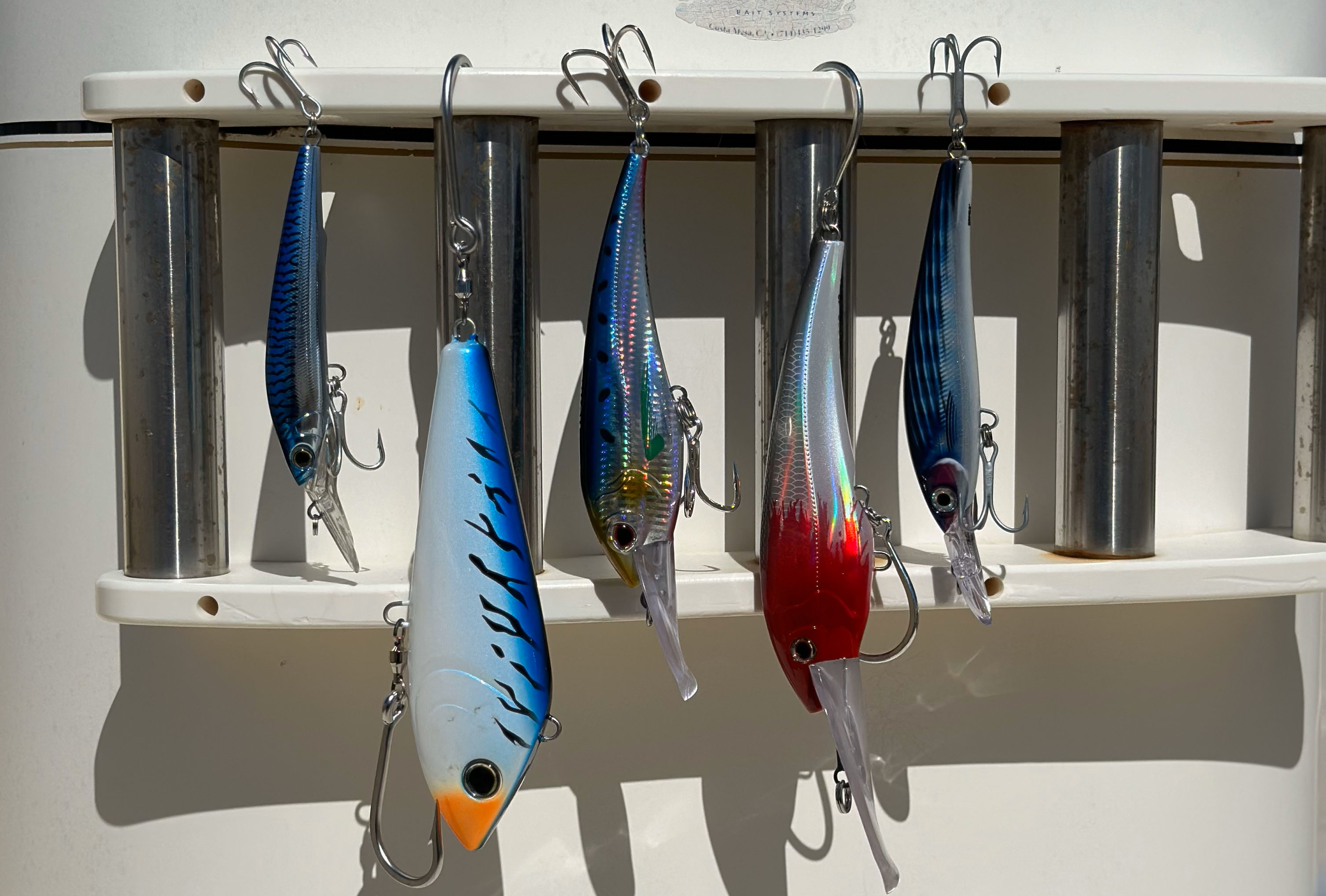 Several lures are hanging off a shelf. Lures are mainly blue, with one being red and white.