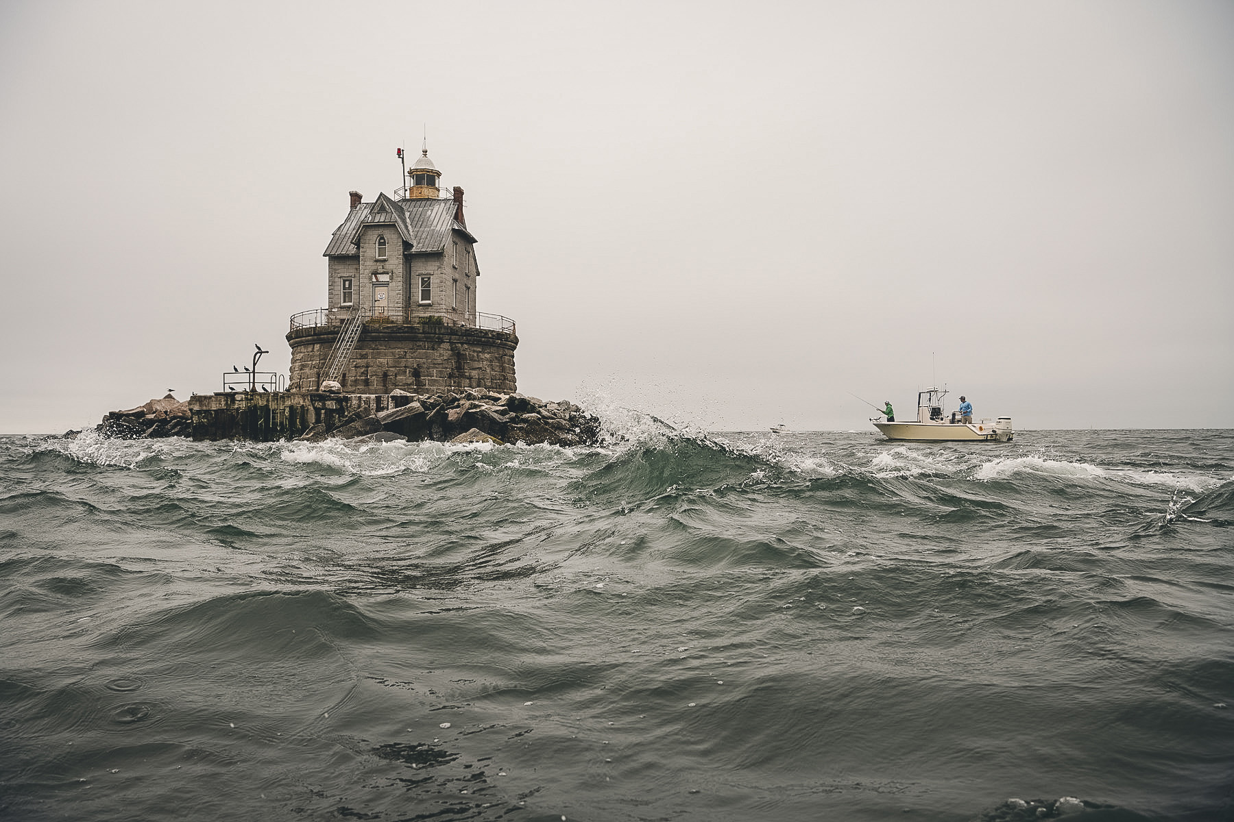 A house-like structure built on a rocky reef, surrounded by rough sea water.
