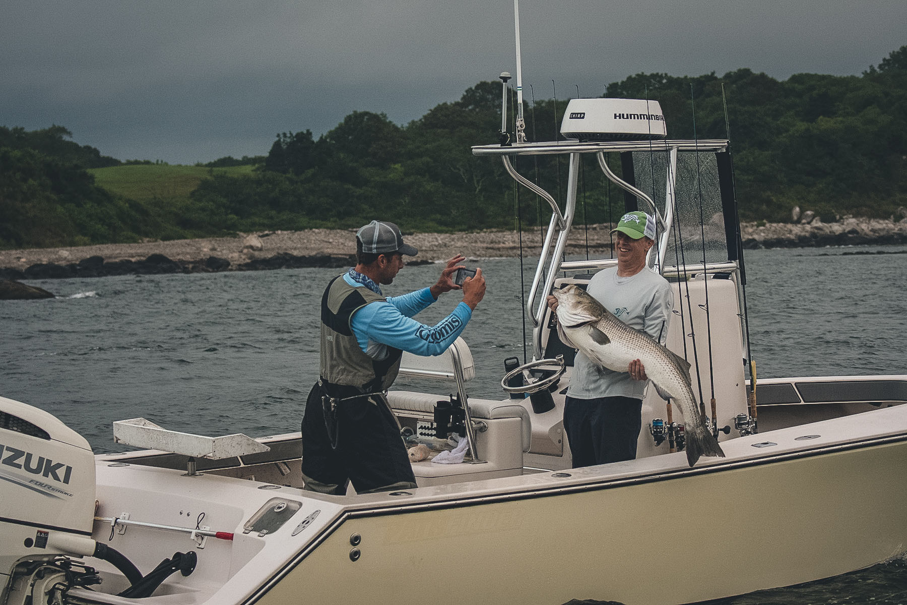 Two people are standing on a boat, one holding a fish and the other taking a picture.