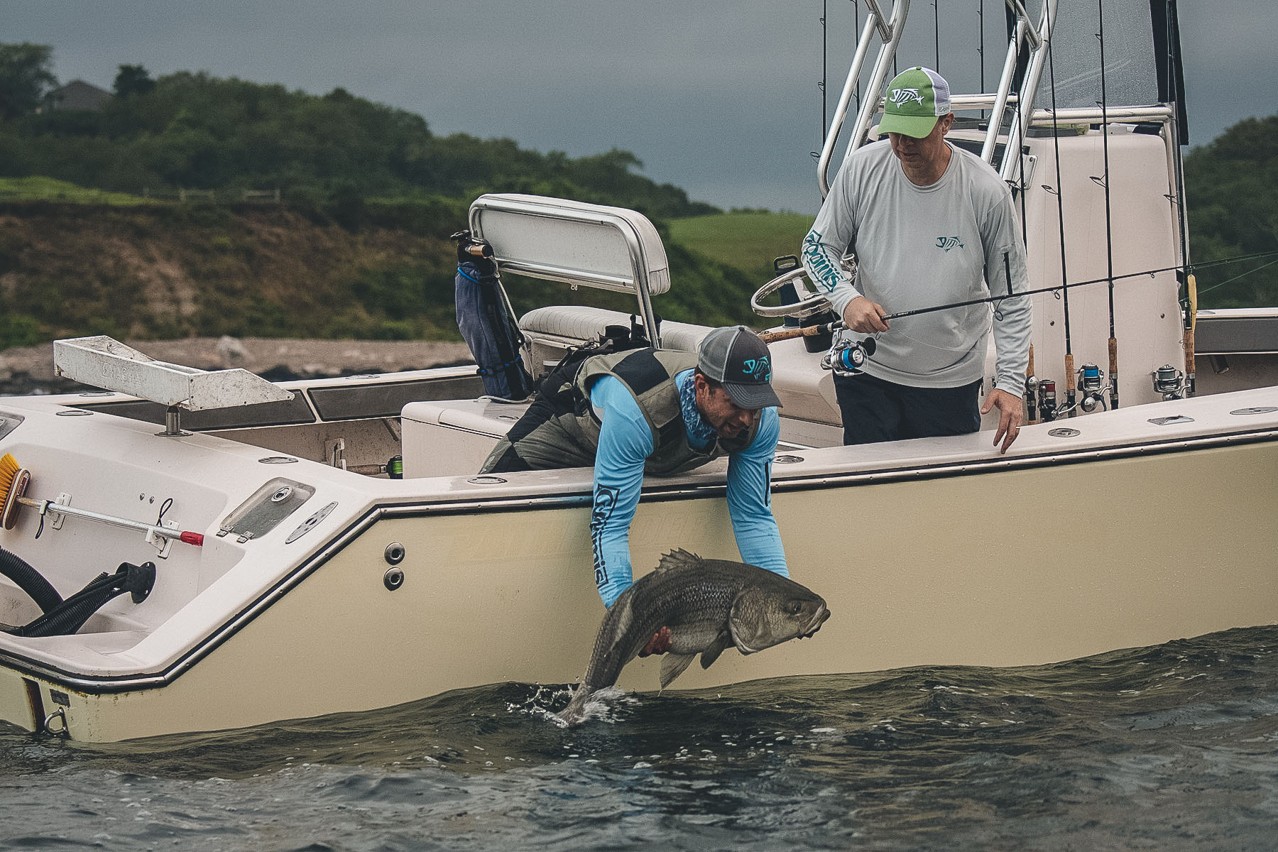 Two people are standing on a boat, one is putting a fish back in the water while the other watches.