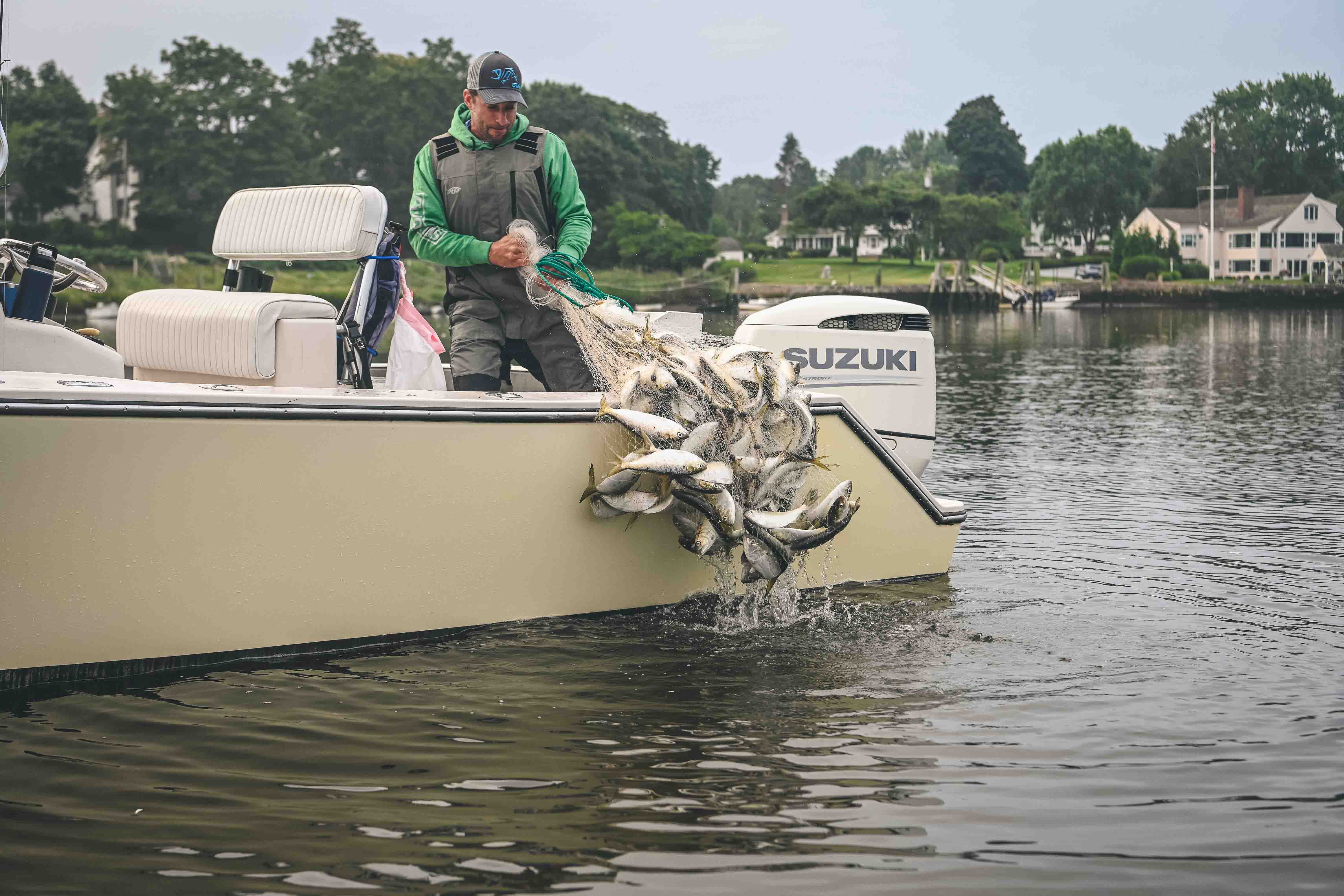 A person is standing on a boat, pulling in a net full of fish.