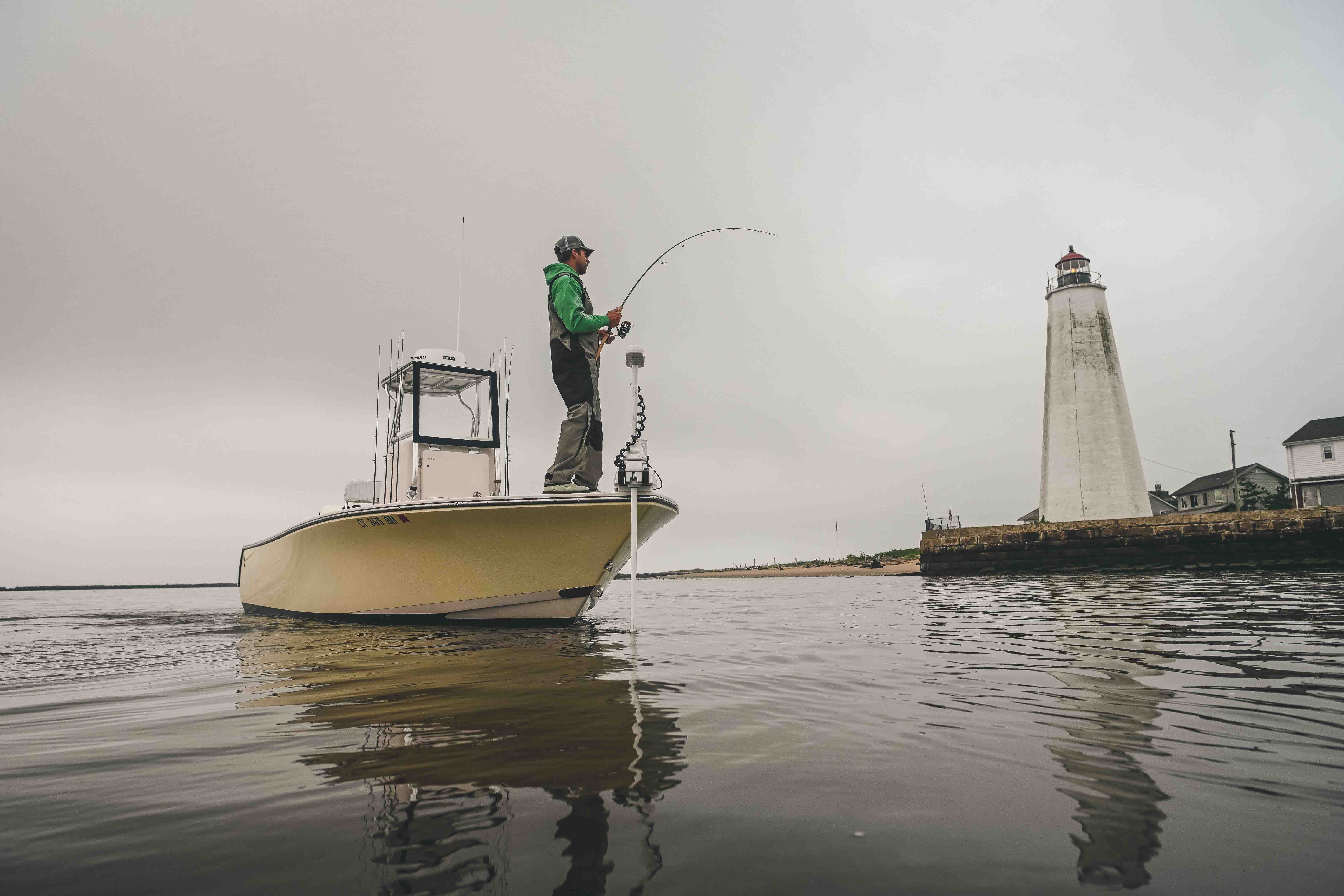 A person is fishing from a boat near a lighthouse.