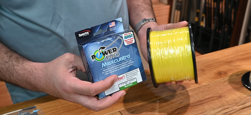 Person holding a blue box of PowerPro Maxcuatro braided line box and a large spool of bright yellow line.