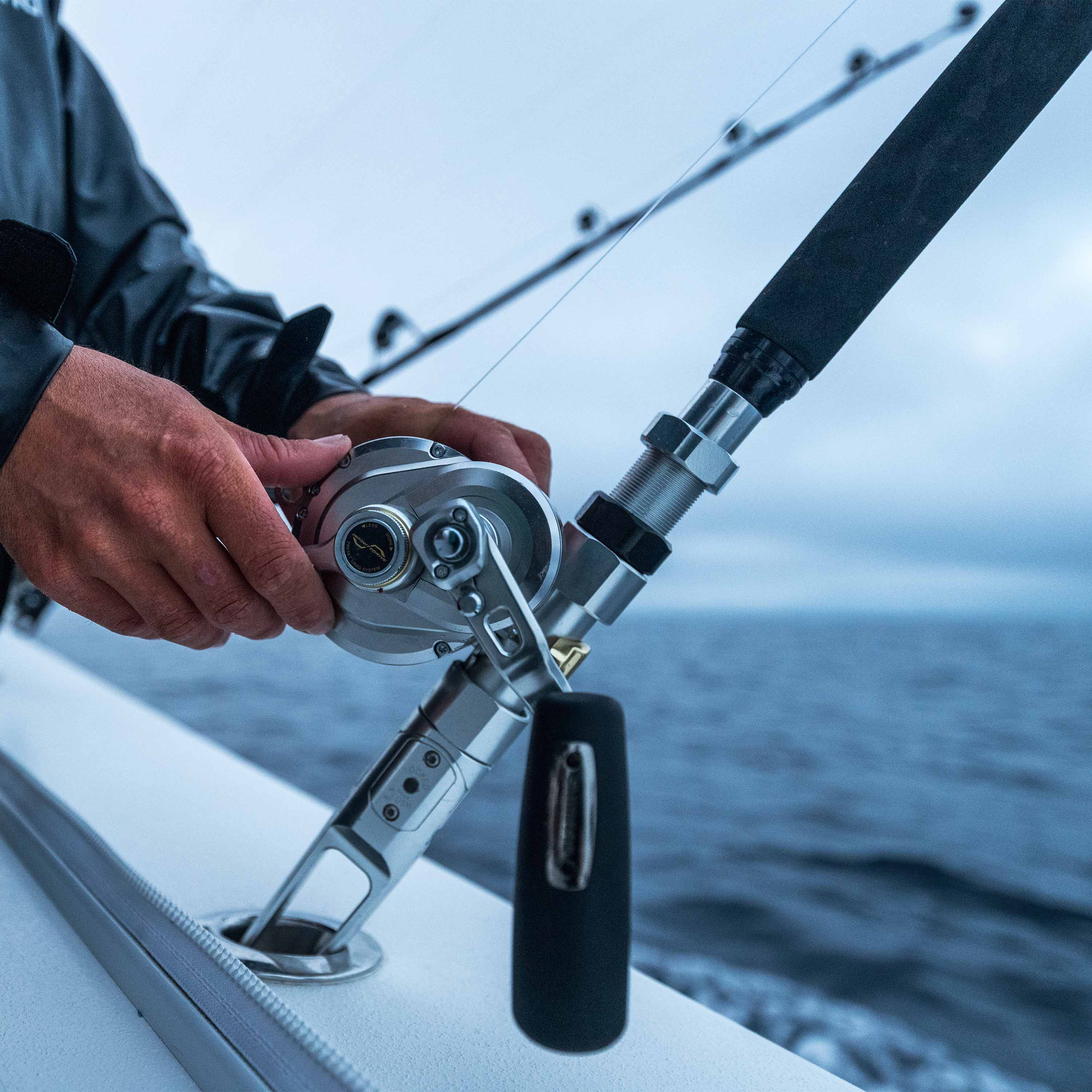 Close-up of an angler adjusting a conventional offshore fishing reel and rod while trolling on the ocean during an overcast early-season Pacific bluefin tuna trip.
