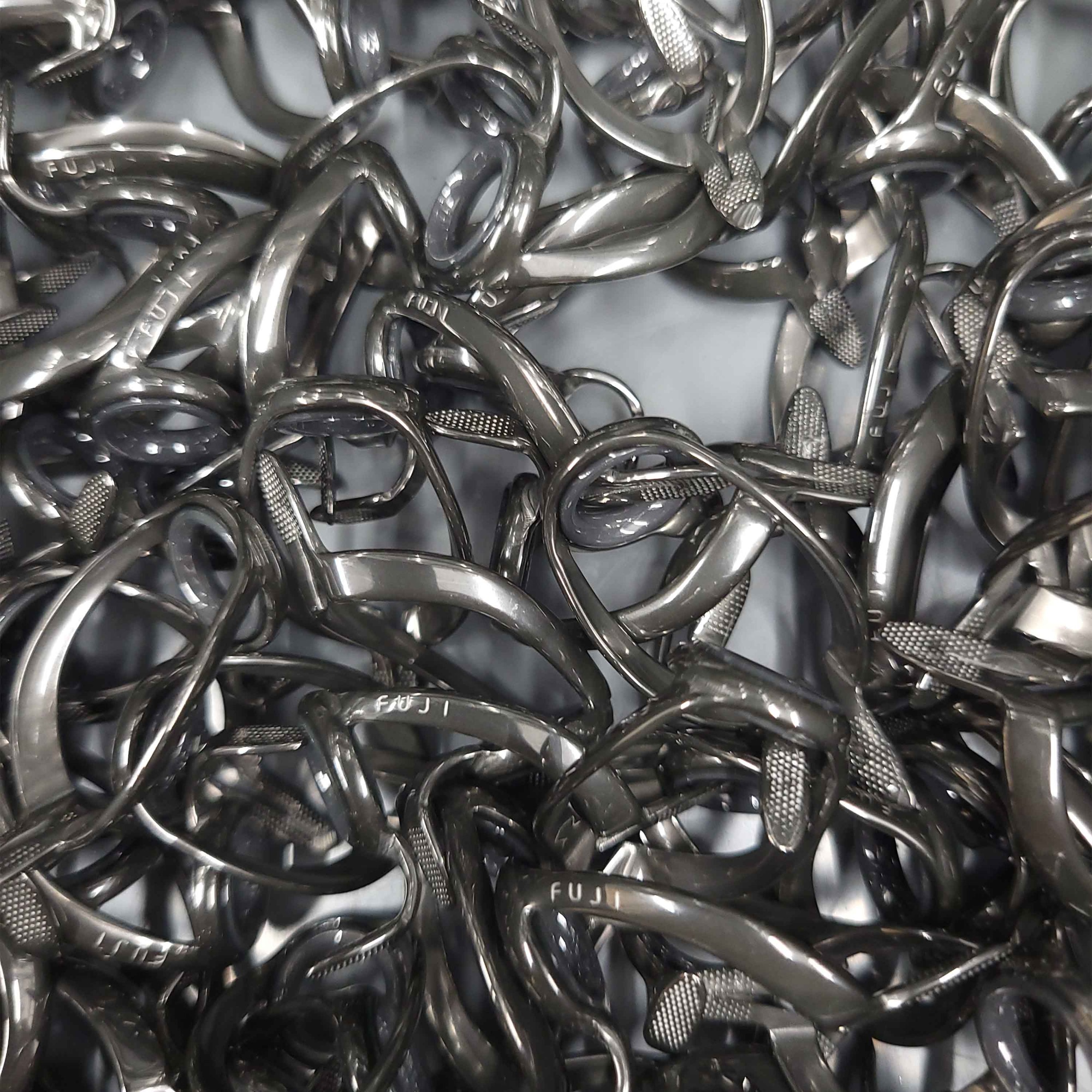 Pile of metal Fuji ring guides with textured feet and ceramic inserts, stacked in a bin ready for fishing rod assembly.
