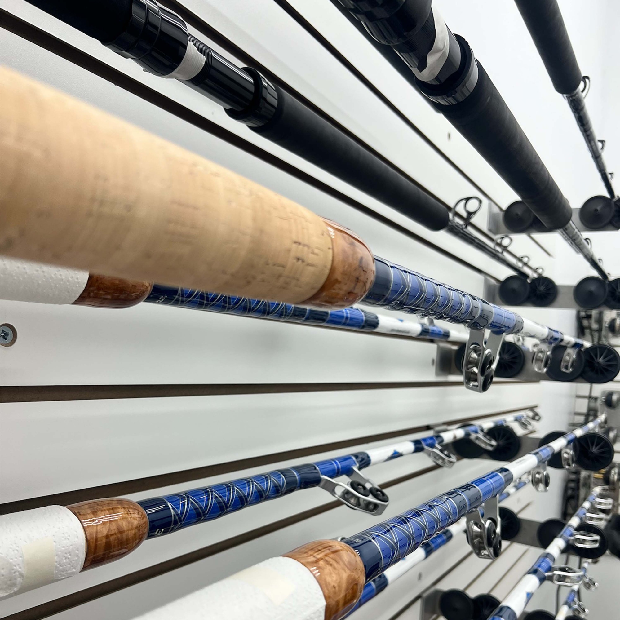 Melton Tackle custom rods with blue thread wraps and cork handles displayed on slatwall inside the Melton Tackle Rod Shop.