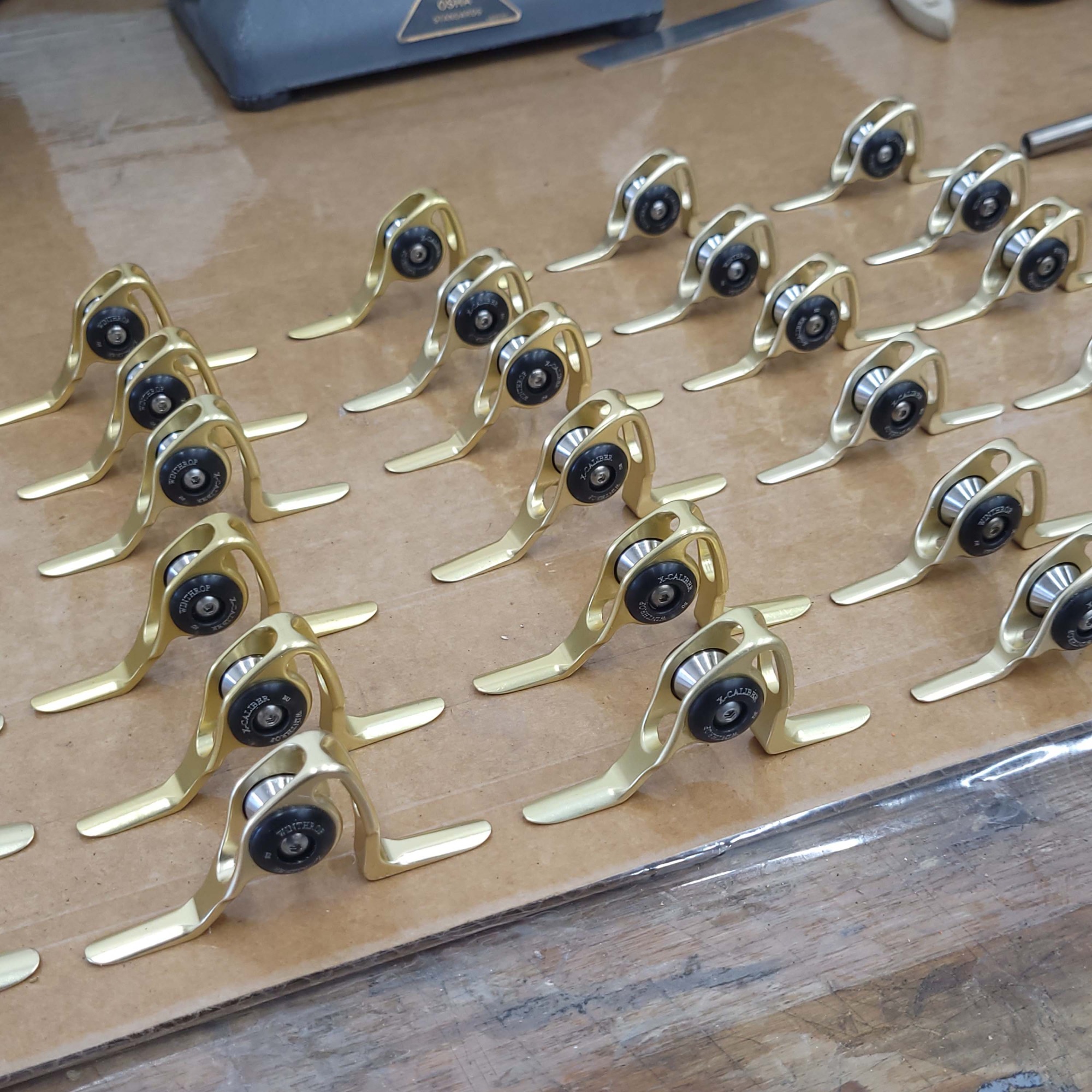 Rows of gold roller guides with black bearings neatly arranged on a cardboard surface, ready for assembly on heavy-duty fishing rods.