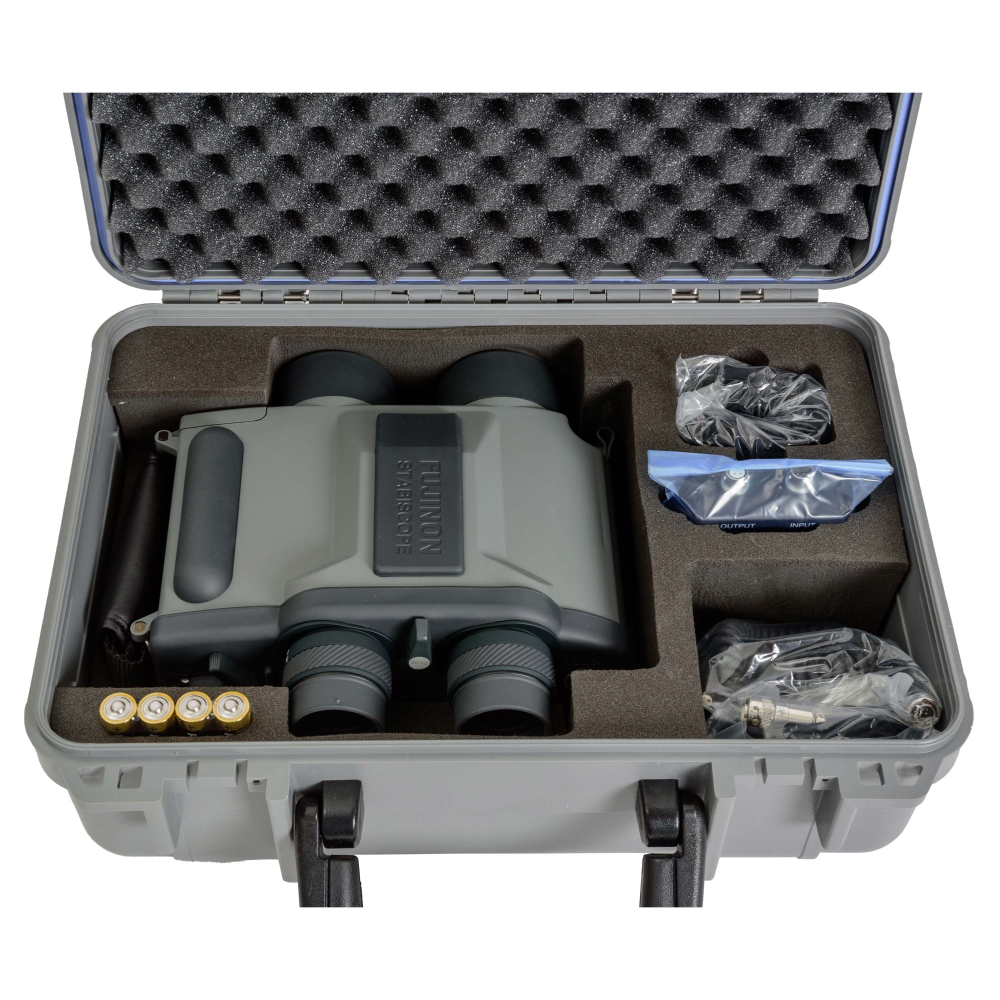 Open storage box containing a pair of gyroscopic binoculars, batteries and gyro accessories. The binoculars are a greenish gray, with some darker parts in gray and black.