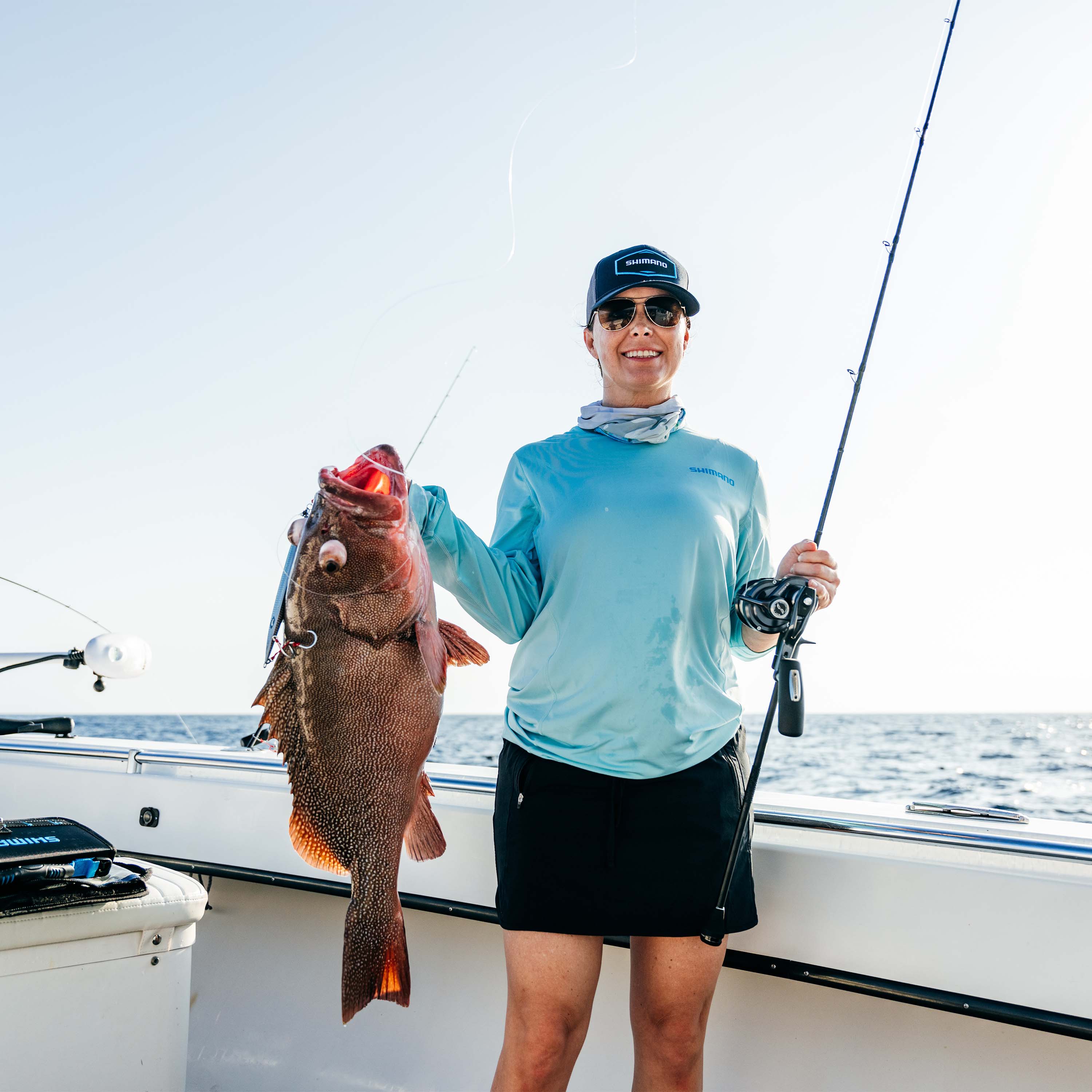 Person standing on a boat holding a fishing rod and a large fish with a Shimano Sardine Waver lure attached.
