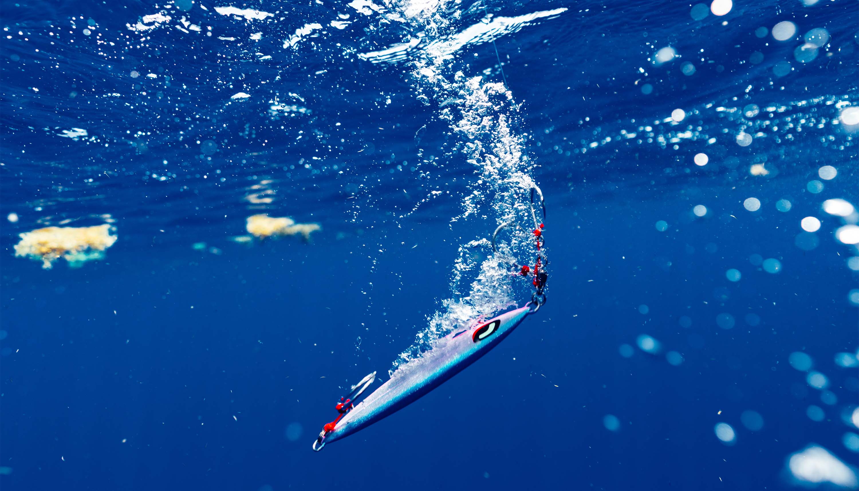 Shimano Sardine Waver fishing lure suspended underwater beneath the surface, surrounded by bubbles in deep blue water.