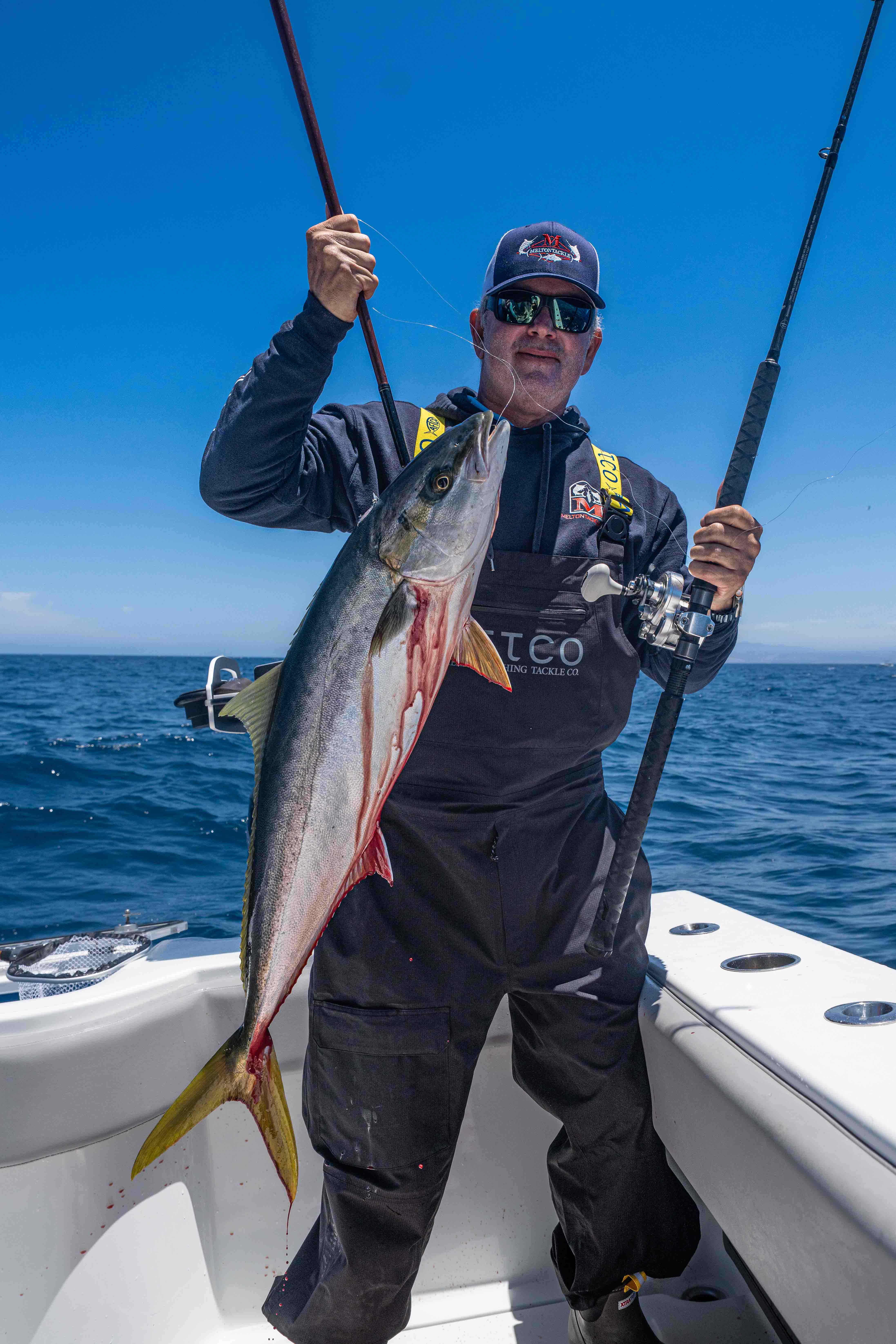 Wintertime Yellowtail on Artificials - Tracy Melton holds a yellowtail and fishing rods aboard a boat on the ocean.