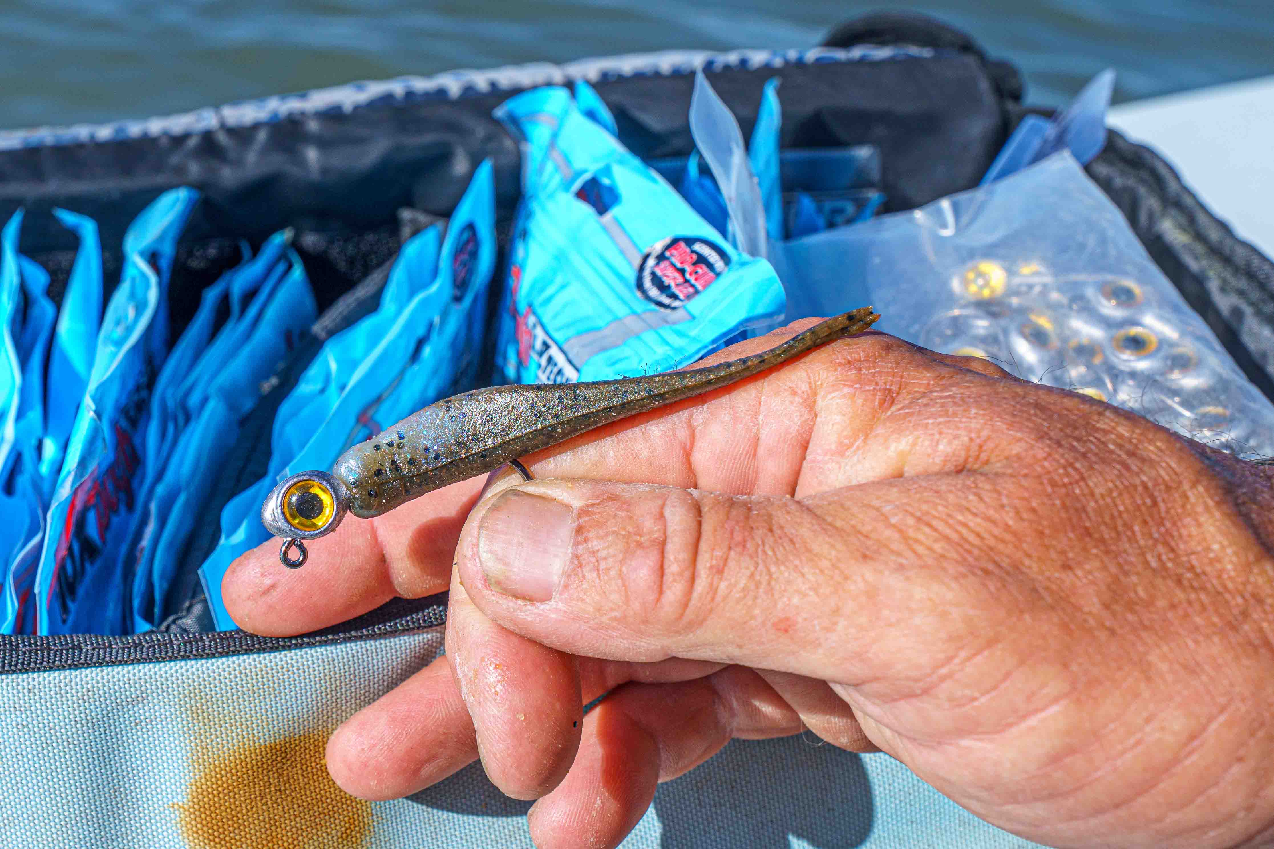 Close-up of a hand holding a Z-Man soft plastic paddle tail lure rigged on a jighead beside tackle bags on a boat.