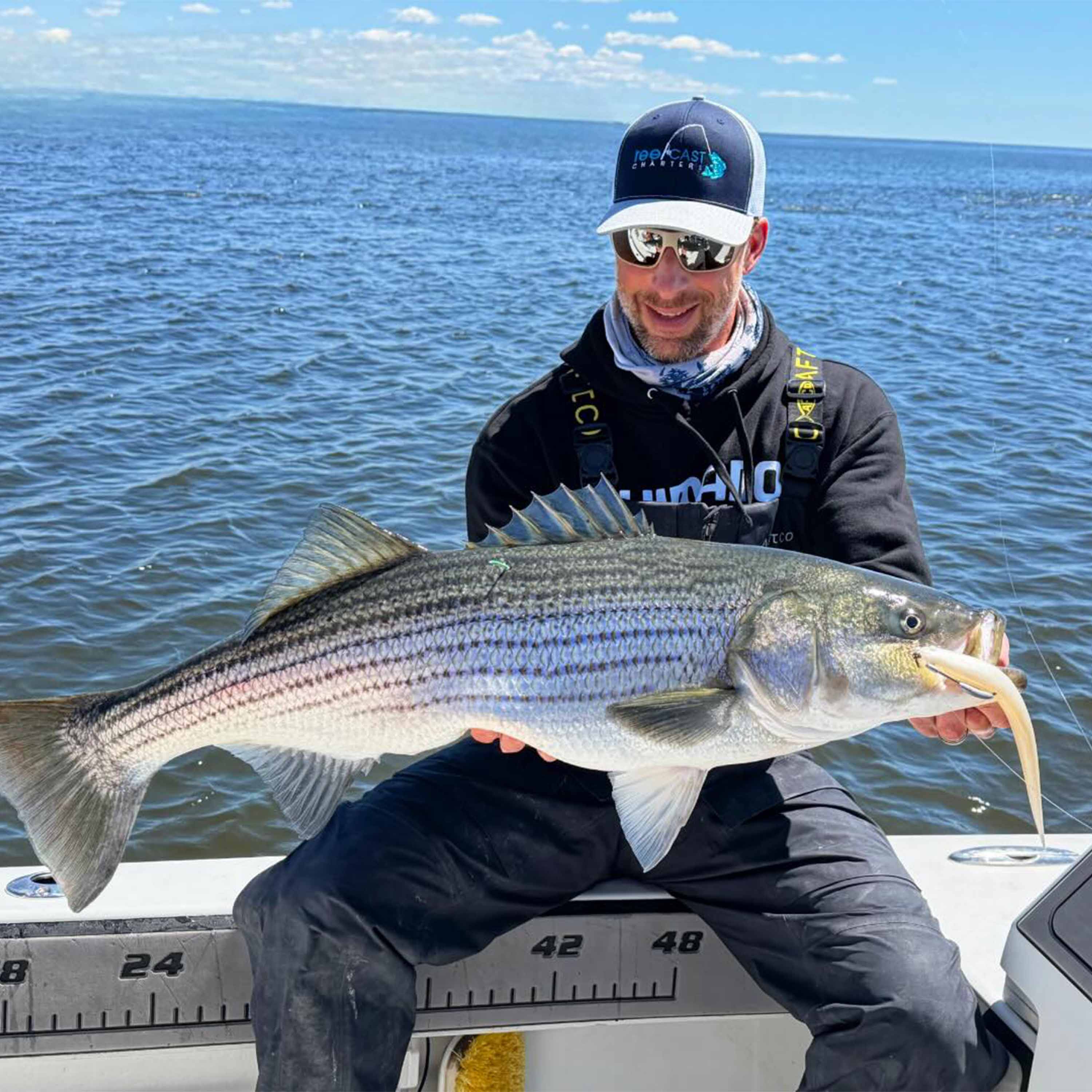 Captain Mike Roy holding a striped bass with a soft plastic lure aboard a fishing boat on Connecticut waters